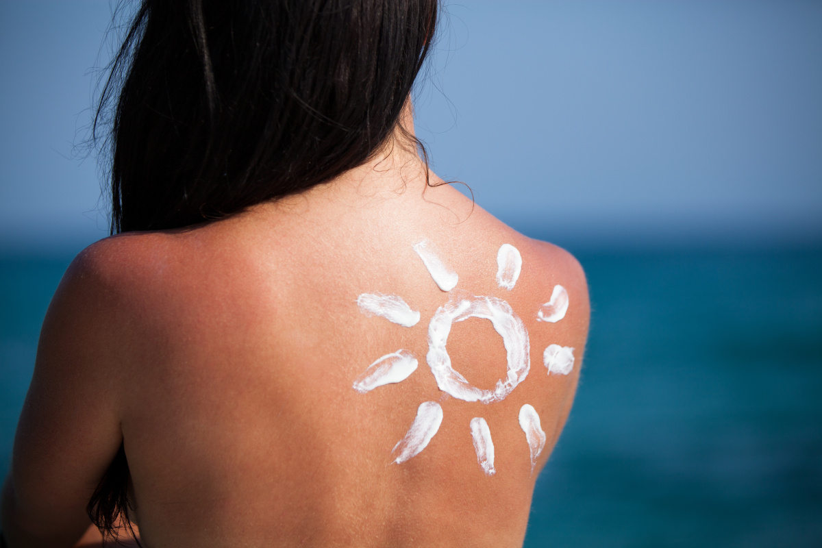 Eine Frau sitzt am Meer in der Sonne. Ihr Rücken ist mit Propolis Salbe eingecremt.