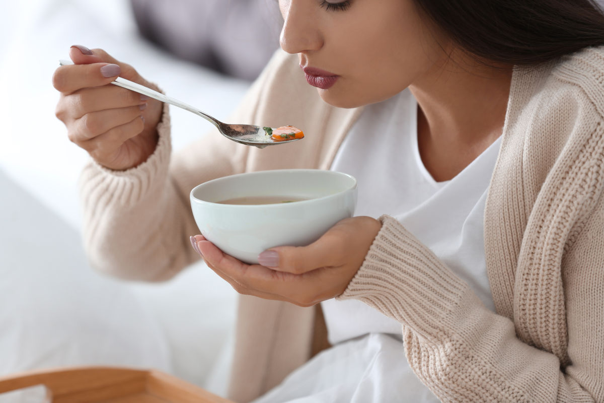 Frau löffelt Hühnersuppe bei Magen-Darm-Problemen